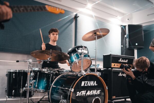A young drummer practicing with a band in a modern music studio.