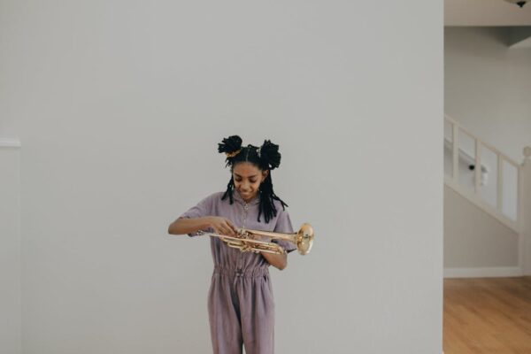 A young girl with braided hair smiling while holding a trumpet in an indoor setting.