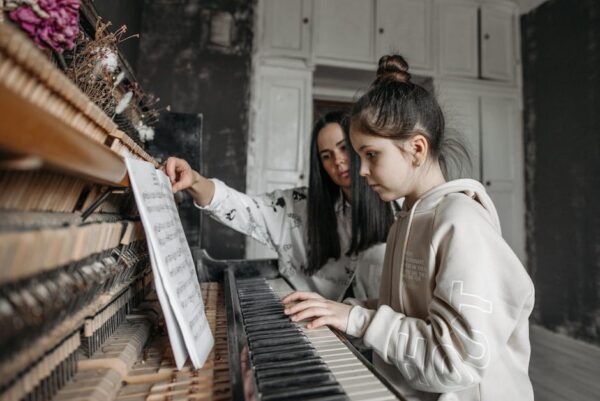 Young girl learning piano with her teacher in a music studio, focusing on sheet music.