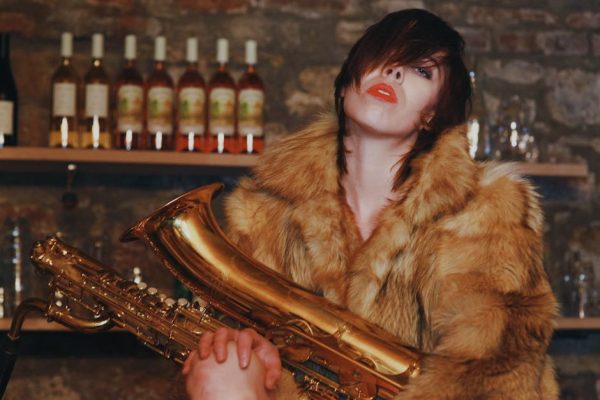 Fashionable woman posing with saxophone in a bar, surrounded by bottles. Bold and artistic vibe.