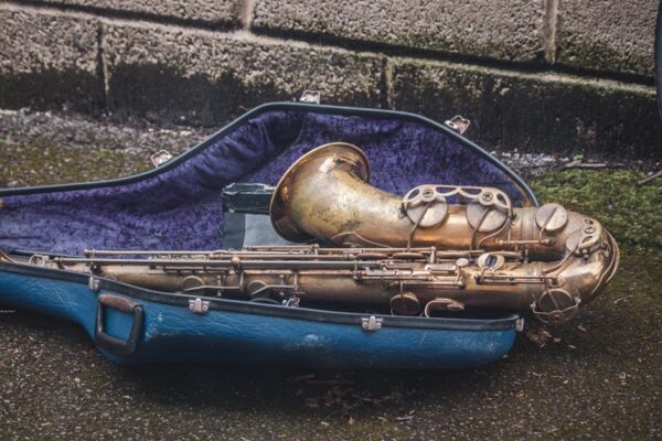 Close-up of a vintage saxophone lying in an open blue case against a weathered stone background.