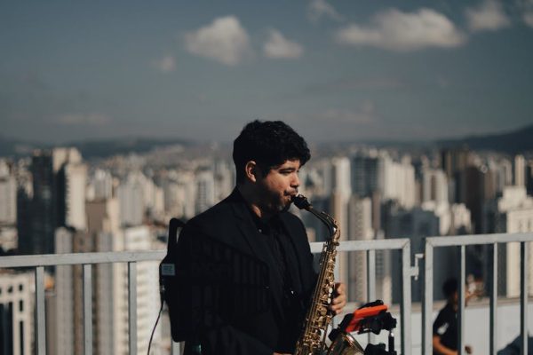 Musician playing saxophone on a city rooftop with urban skyline in the background.