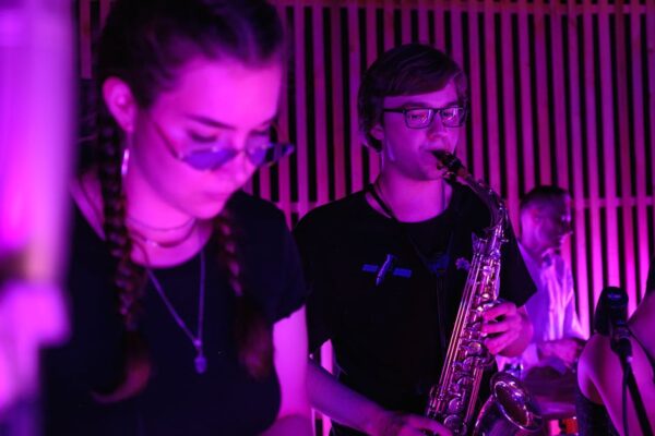 A captivating indoor music performance featuring a saxophonist in vibrant purple lighting.