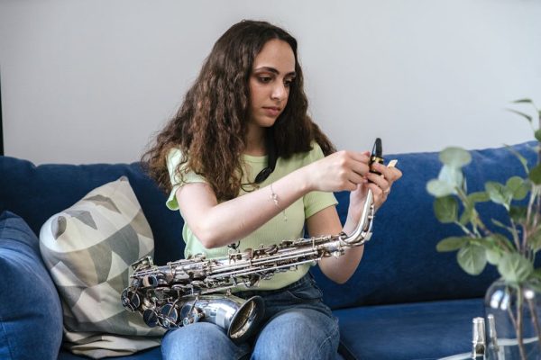 A young woman assembles her saxophone while sitting on a blue sofa in a cozy indoor setting.