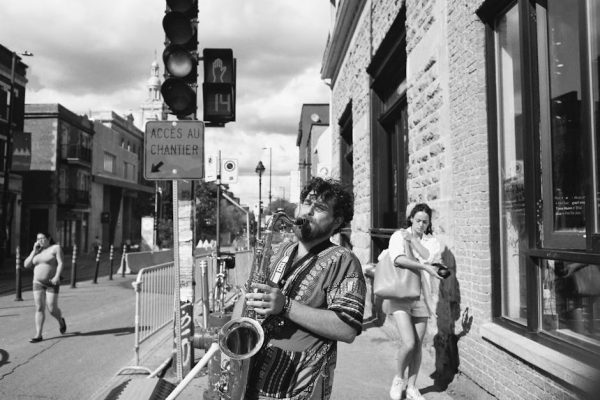 Black and white photo of a street musician playing saxophone on a lively street in Montreal.