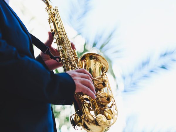 A musician in a suit plays a golden saxophone against a bright sky, showcasing musical talent and outdoor ambiance.