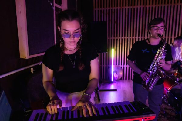 Musicians rehearsing with keyboard and saxophone under colorful lights.