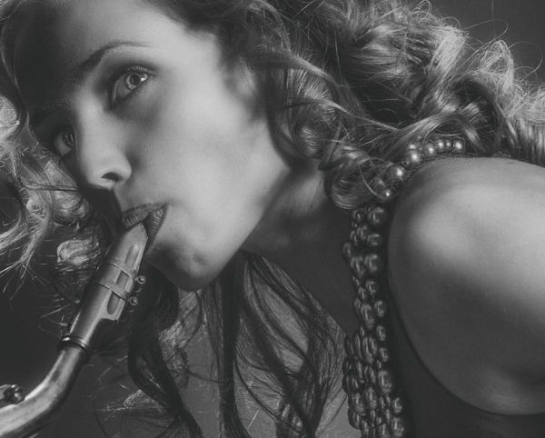 Black and white close-up portrait of a woman playing the saxophone, capturing her expression.