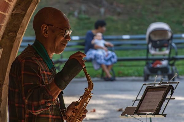 A street musician plays saxophone in a park, captivating his audience.