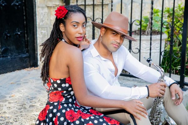 Elegant couple poses with saxophone in a charming outdoor setting, embodying style and musical flair.