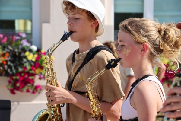 Two teenagers playing saxophones in an outdoor summer performance, vibrant and lively.