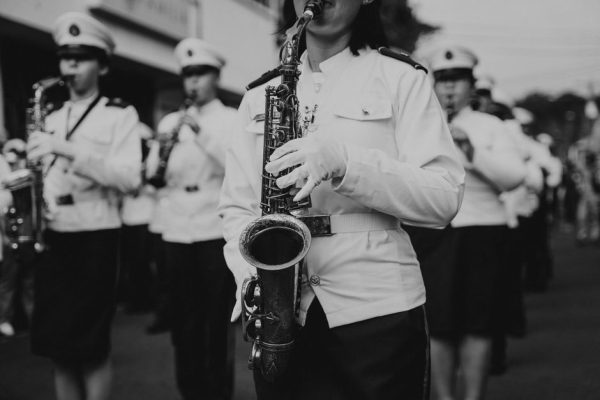 A black and white photo of a marching band performing in uniform during a parade.